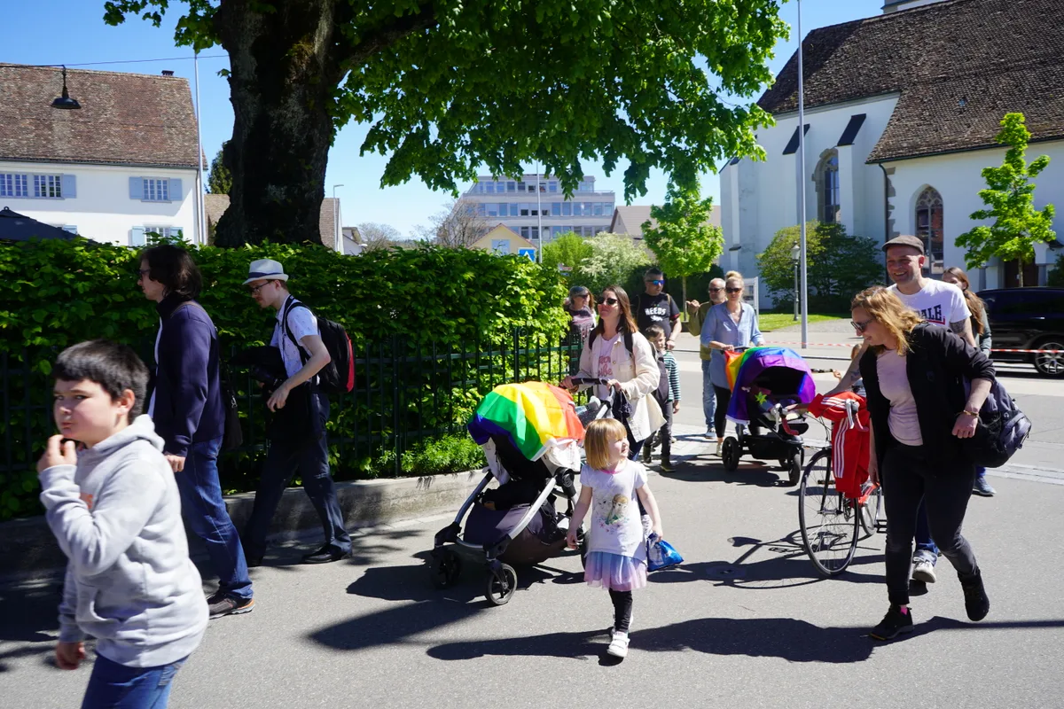 Man sieht Familien mit Kindern. Ein Kinderwagen ist in eine Regenbogenfahne gehüllt.
